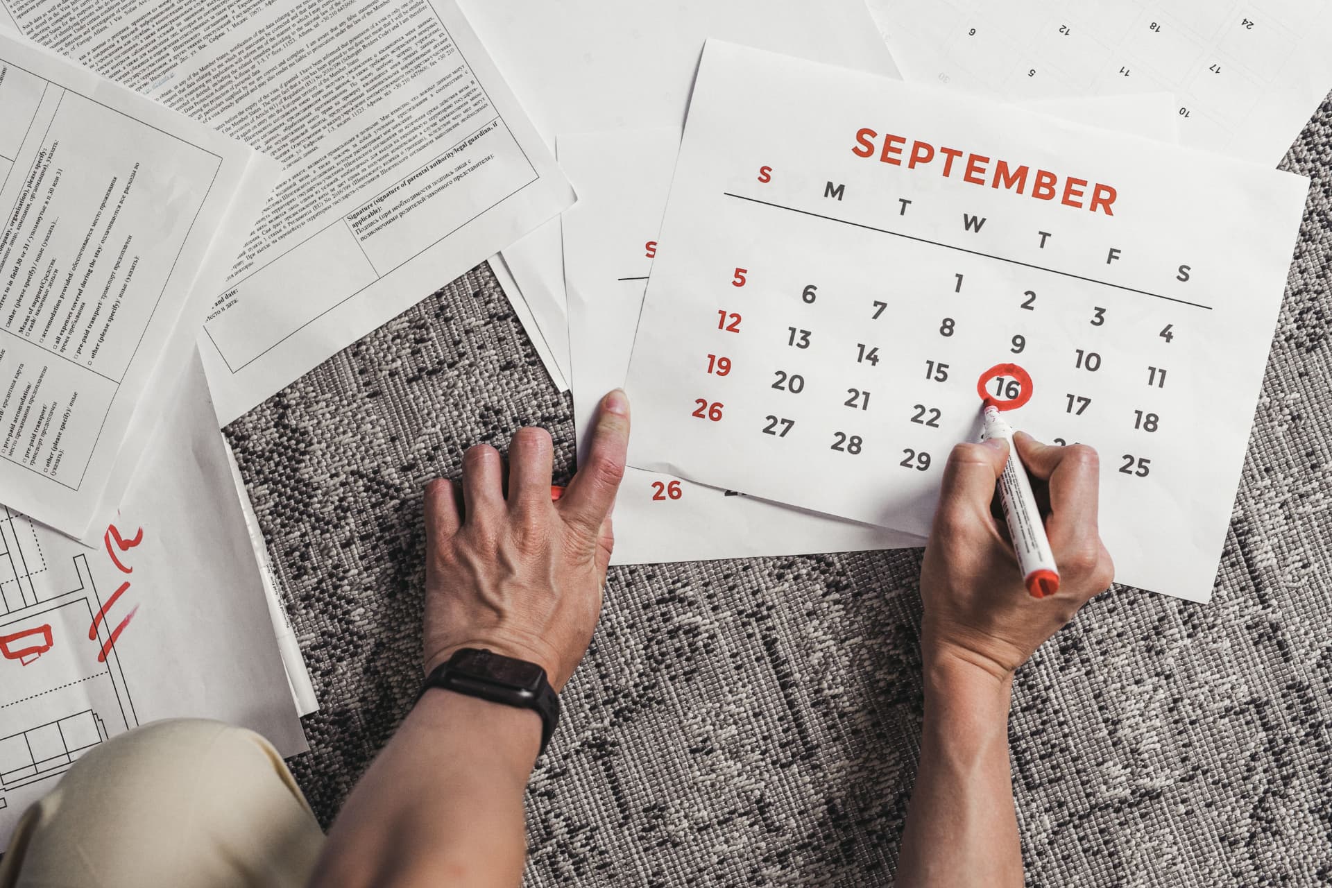 Une personne entoure une date sur un calendrier de septembre posé parmi des documents.