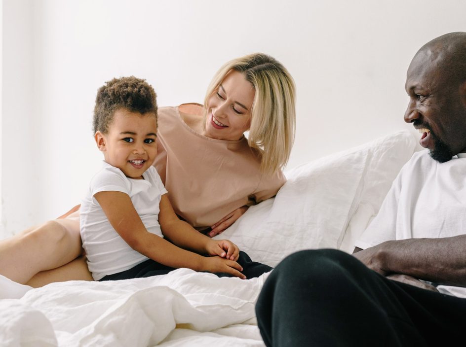 Une famille sourit ensemble sur un lit, la mère, le père et leur enfant